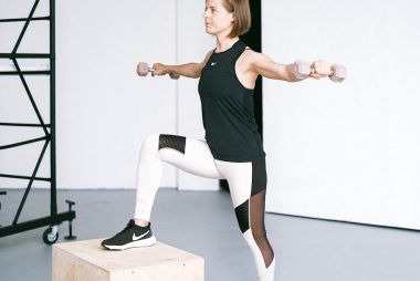 Woman performing fitness exercise with dumbbells in a gym setting, showcasing strength and balance.